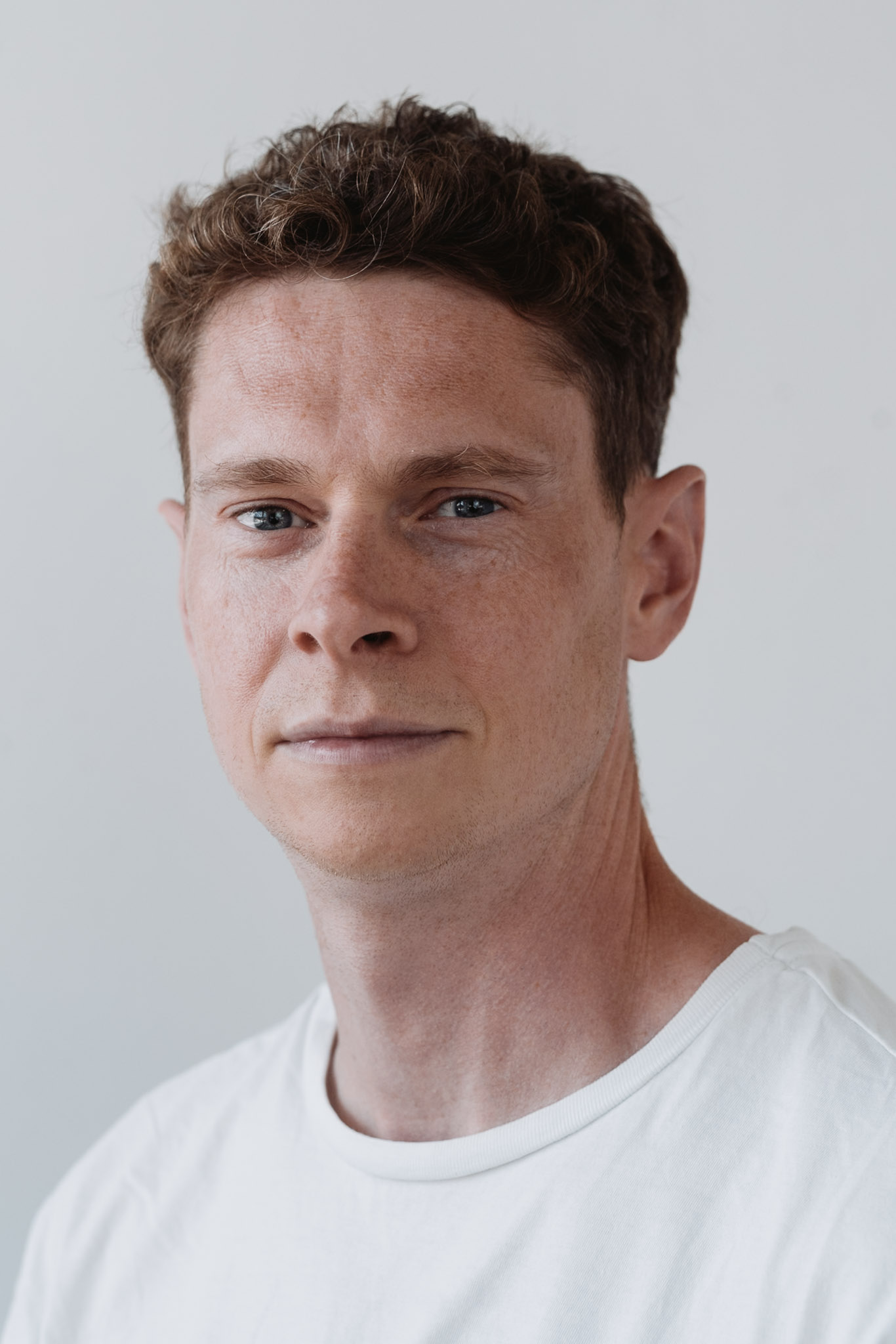 Corporate headshot — man in white, minimal clean background.