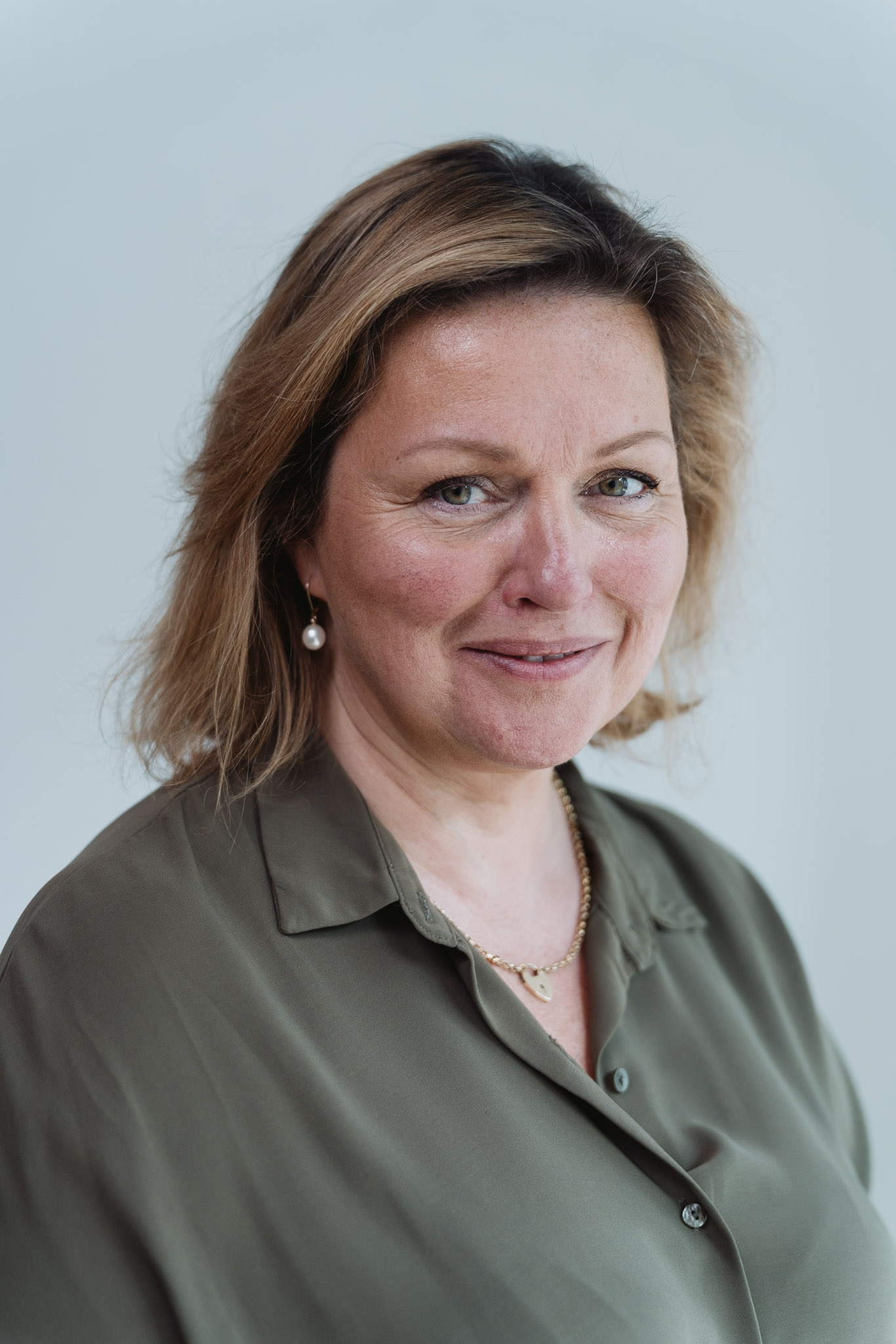 Professional headshot — woman in olive, soft natural expression.